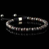Lukze faceted bronzite and pyrite macramé bracelet on a black reflective surface